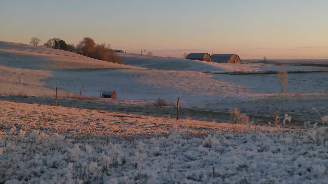 Showing frosty rural hills warming with low sun, mist drifting past barns and shed
