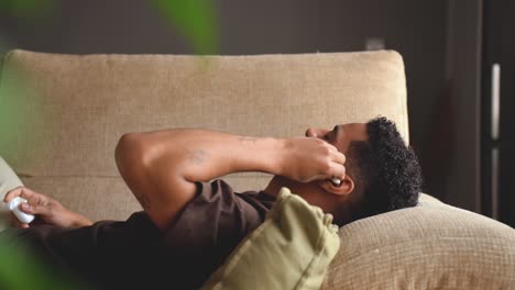 Calm-ethnic-man-sleeping-in-earphones-on-sofa