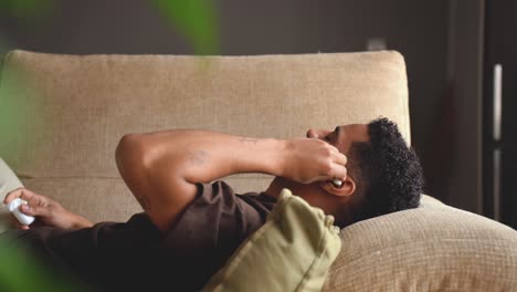 calm ethnic man sleeping in earphones on sofa