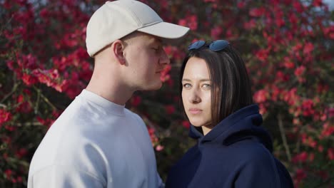 couple stand near chinese quince shrub, guy give kiss on girlfriends forehead