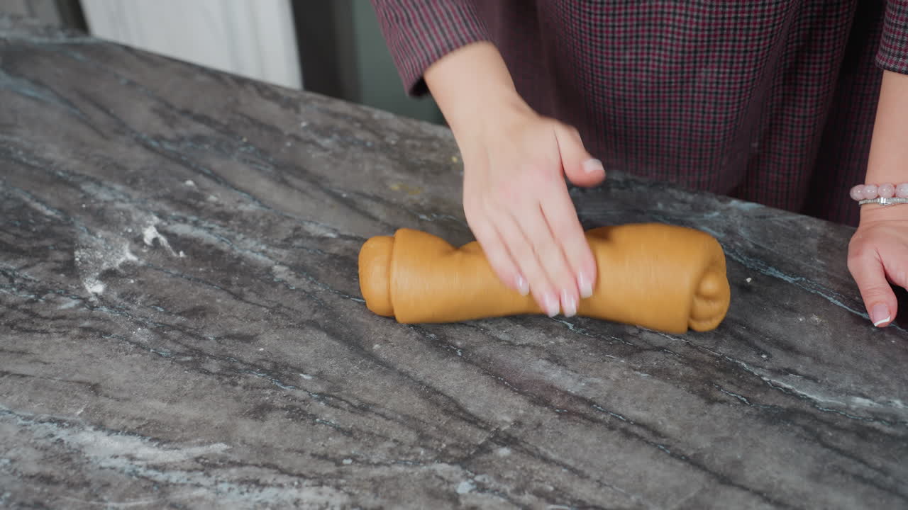 primer plano de una chef femenina con una pulsera en la muñeca izquierda ajustando y amassando masa fresca en el mostrador de la cocina con un fondo borroso que muestra una cocina moderna y una cálida y acogedora iluminación interior