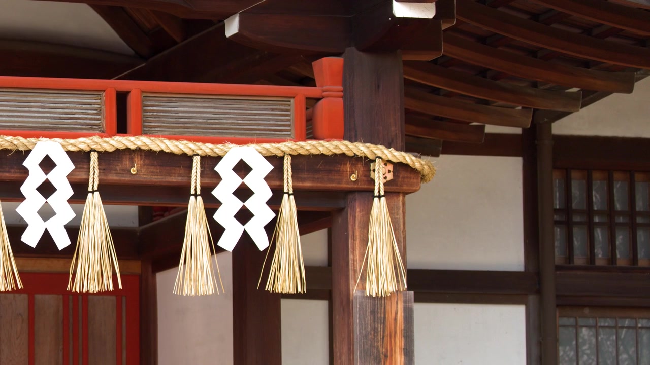 Static medium shot of sacred straw rope and paper streamers on a wooden temple structure.