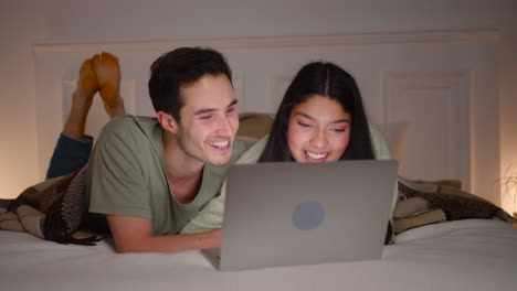 close up view of a couple watching interesting movie on laptop lying in bed at home