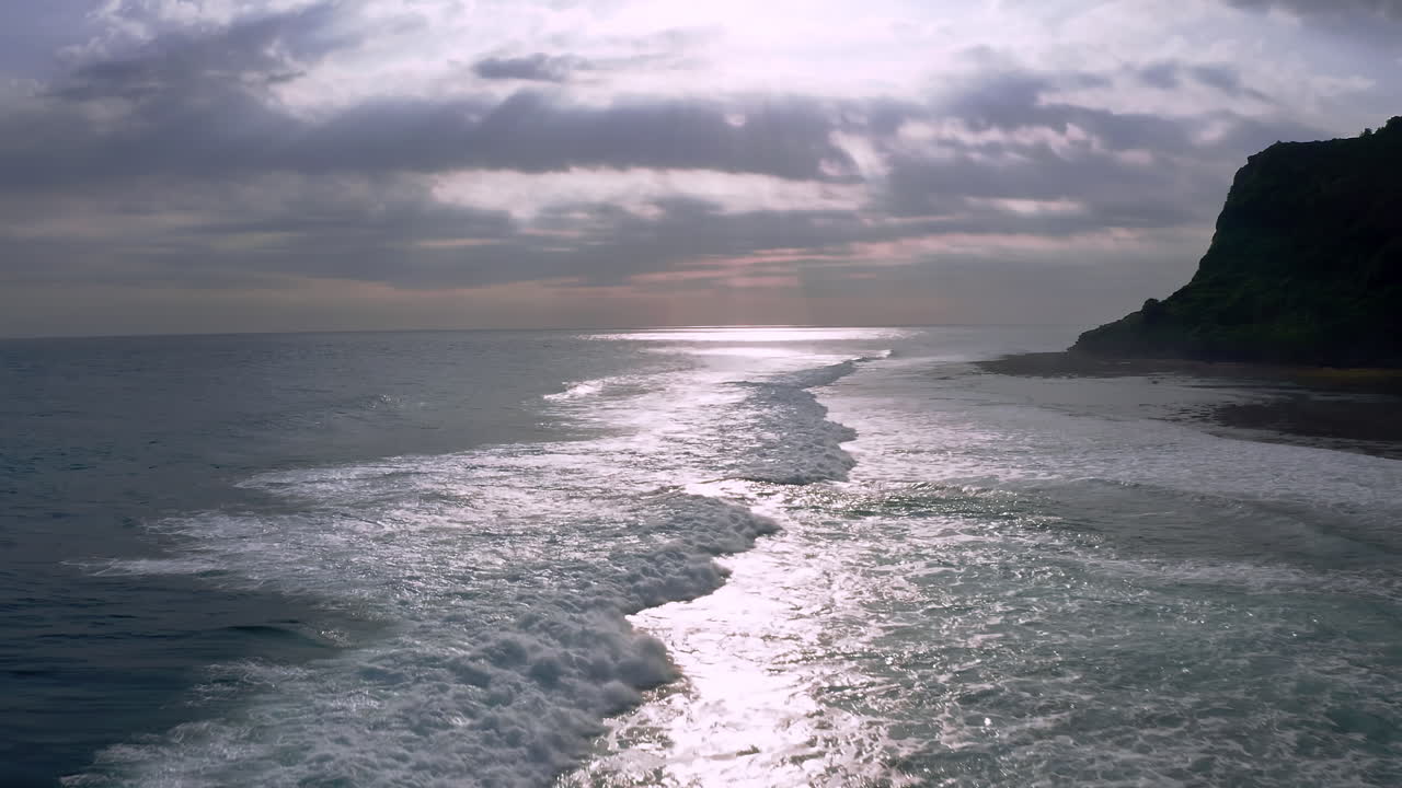 olas marinas espumosas lavando en la orilla con el sol rompiendo nubes por encima