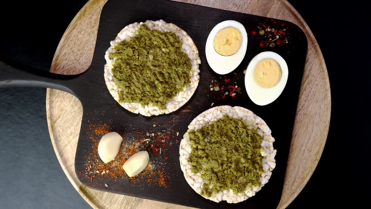 las tostadas de pastel de arroz con salsa de pesto verde y huevos hervidos giran lentamente en la tabla de cortar.