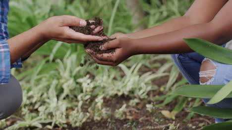 happy african american mother and daughter touching ground in garden, slow motion, unaltered