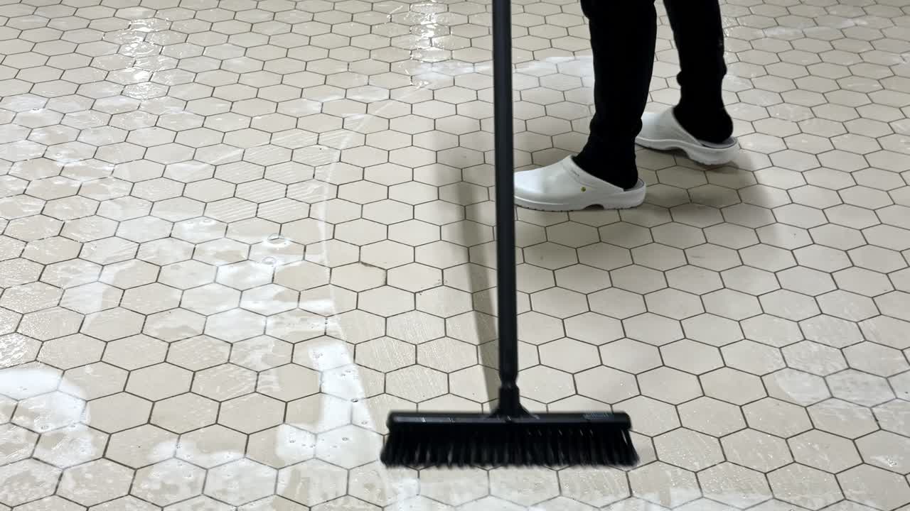A Person Scrubs a Soapy Hexagon-tiled Floor With a Long-handled Brush - Close Up