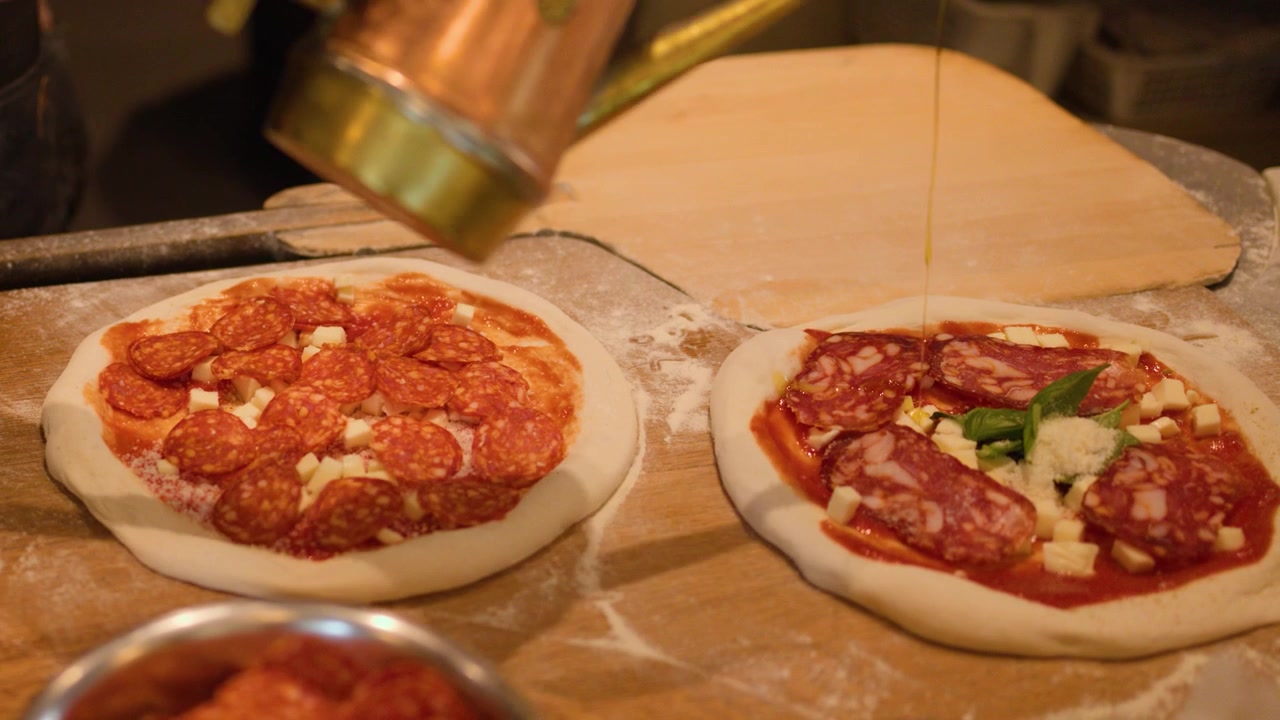 Chef con guanti neri aggiunge pepperoni e olio d'oliva all'impasto crudo della pizza in cucina