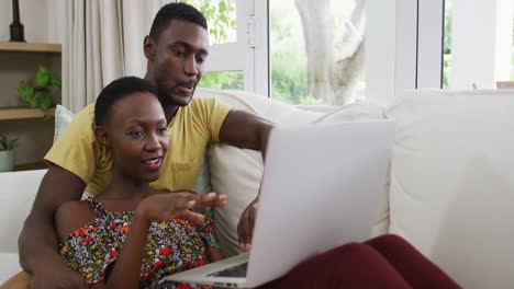 Glückliches-Afroamerikanisches-Paar-Auf-Dem-Sofa,-Das-Sich-Umarmt-Und-Redet-Und-Auf-Den-Laptop-Schaut