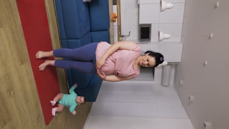 Overweighted-woman-doing-breathe-exercises-while-her-baby-playing-next-to-her