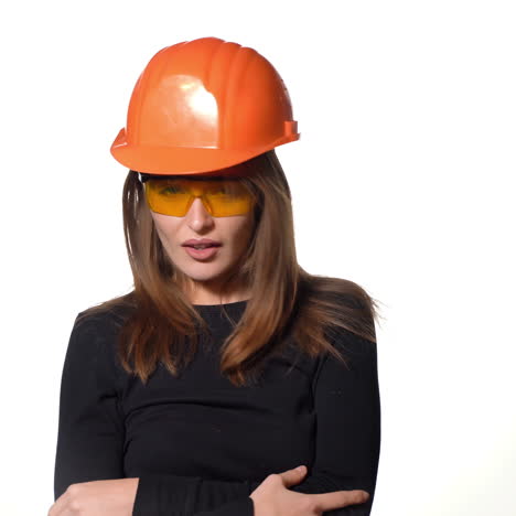 joyful woman engineer in spectacles is standing in an orange helmet and posing on a white background.