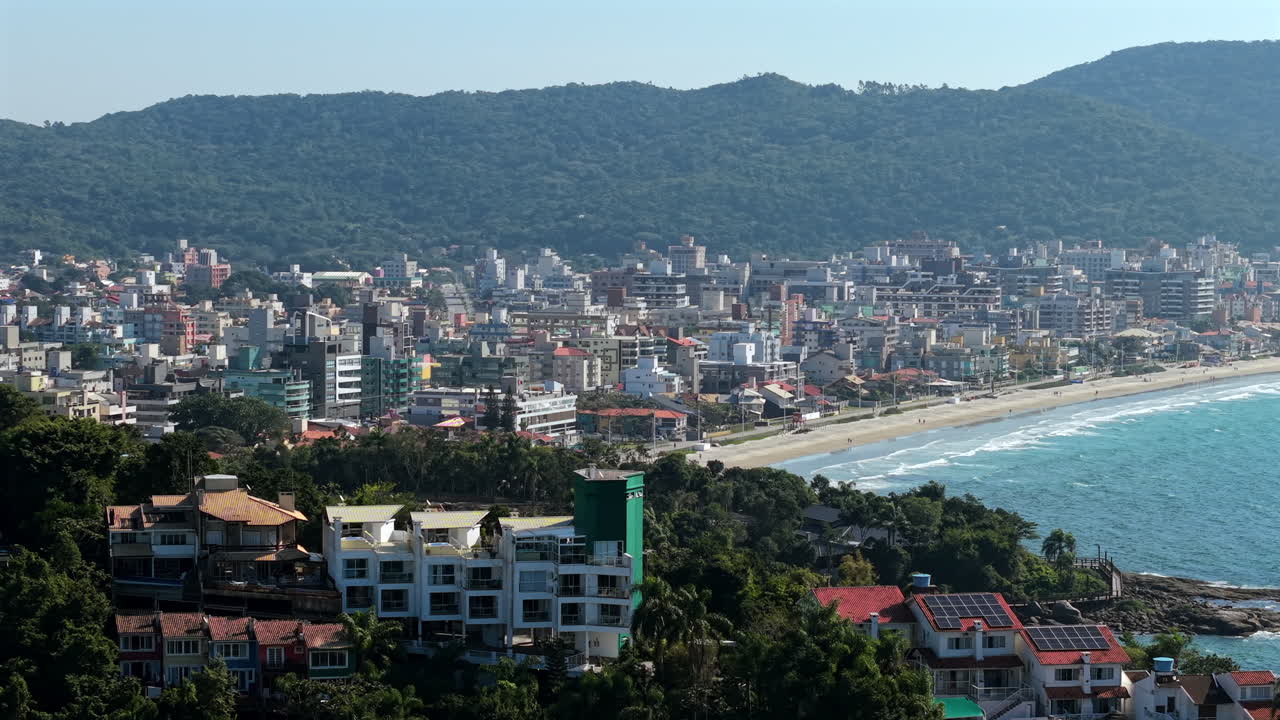 Aerial establishing fly Bombas, Bombinhas beach city with turquoise sea, lush resorts and mountains, Santa Catarina, Brazil