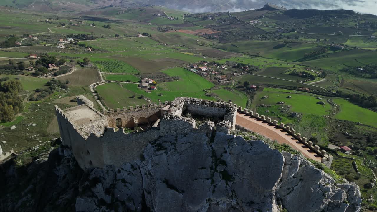 Vista aerea di un antico castello su una scogliera rocciosa, con un paesaggio verde sottostante