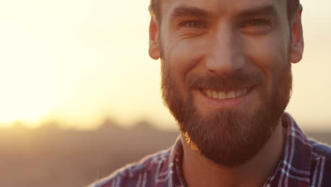 Primer-Plano-Del-Apuesto-Joven-Con-Barba-Sonriendo-A-La-Cámara-Y-Luego-Mirando-Hacia-Abajo-Temprano-En-La-Mañana-En-Su-Campo