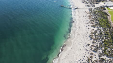 drone aerial panning up over pristine blue water and a white sand beach in australia