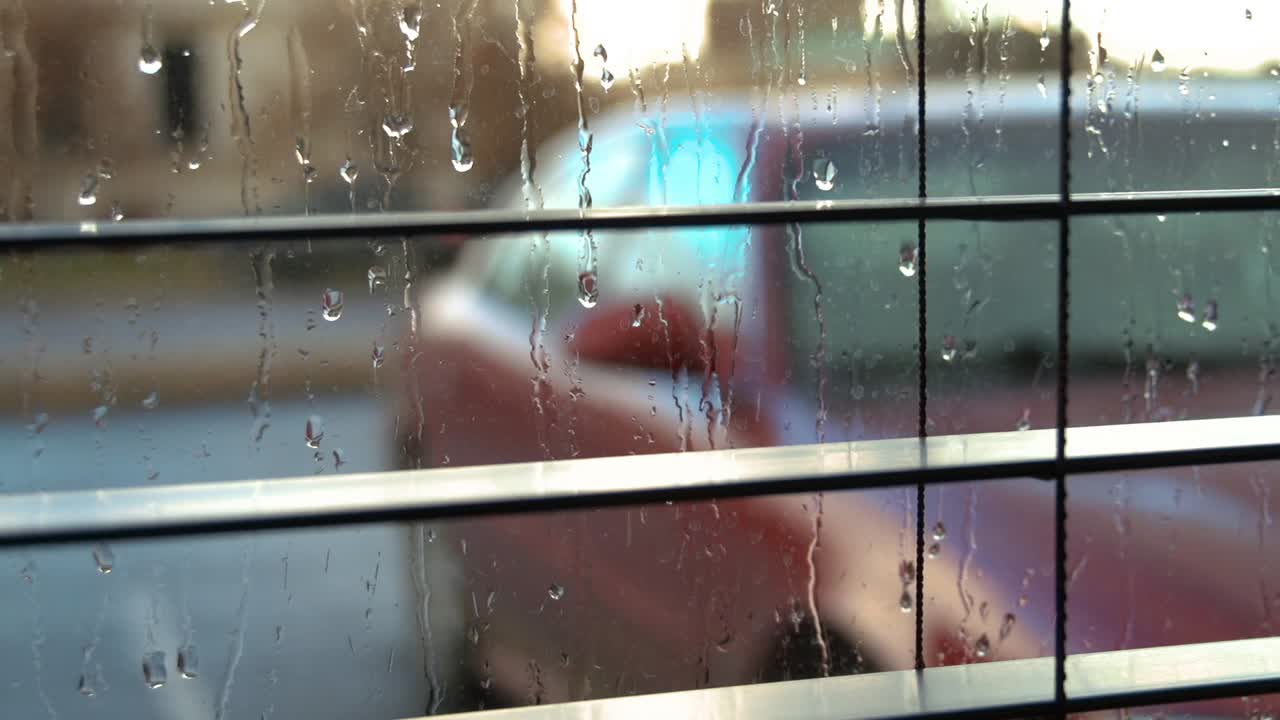 Slow pan from left to right through window blinds at a car in the rain outside