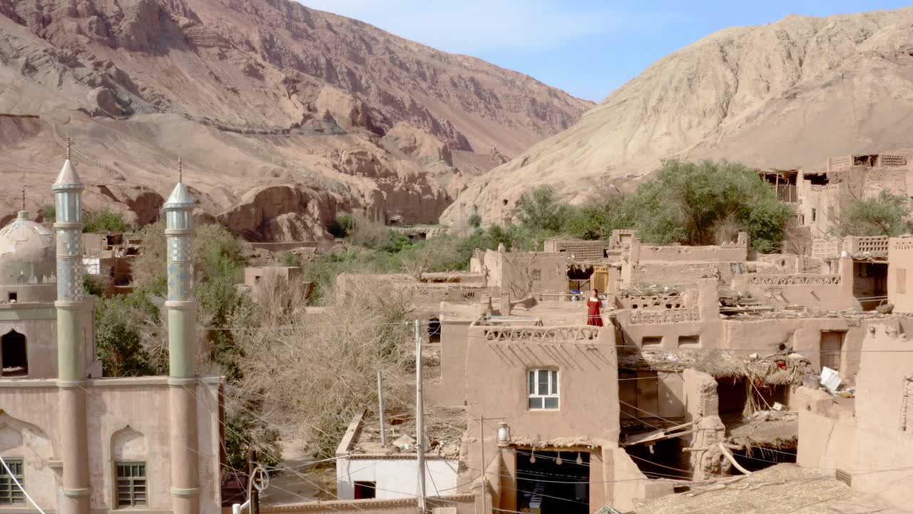 mujer joven con vestido rojo caminando por el techo de una casa de barro en la aldea china rural de tuyoq