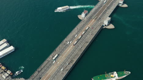 Public-transportation-Tram-Train-passing-Galata-Bridge-over-Bosphorus-in-Istanbul-with-Seagulls-and-Boats-on-water,-Aerial-low-angle-follow-shot