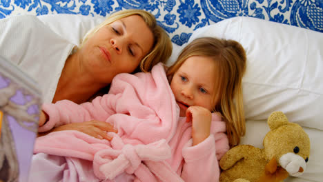 front view of young caucasian mother and daughter reading story book on bed in a comfortable home 4k