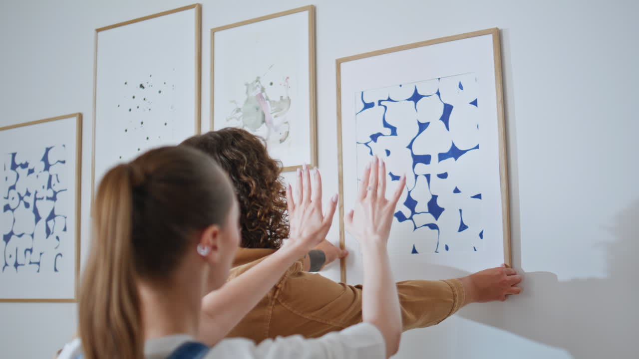 New owners decorating home by hanging posters on wall closeup. Happy couple