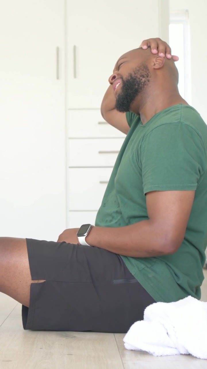 Vertical video: From sweat man in green tee shorts rolling neck then rising in bedroom towel nearby