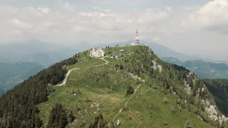 Drone-shot-of-the-mountain-Uršlja-gora,-basking-in-sun,-clouds-and-valley-in-background