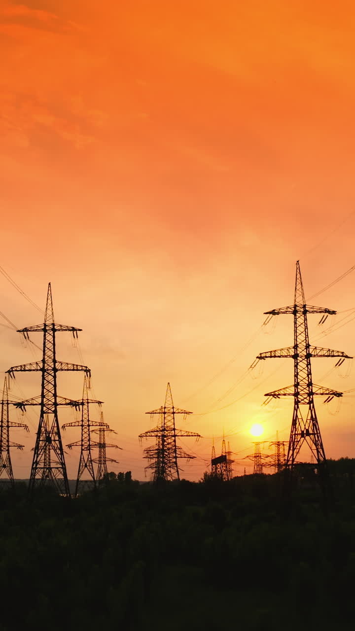 Dark silhouettes of electric towers on red sky background. Transmission lines of high-voltage electric towers at sunset. Vertical video