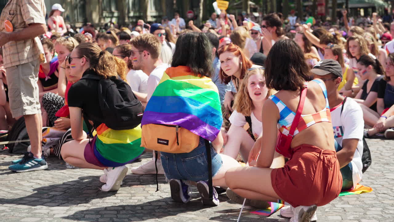 People sitting down in silence in the street behind a vehicle at the Gay Pride march to honor the victims of HIV.