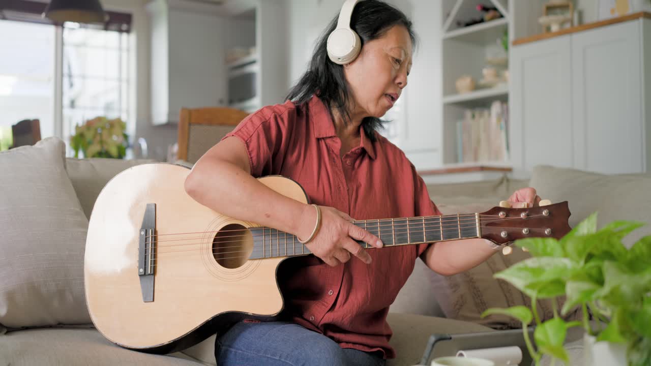 Video verticale: Donna anziana che prende l'accordatore, accordando una chitarra acustica per la musica tramite cuffie.