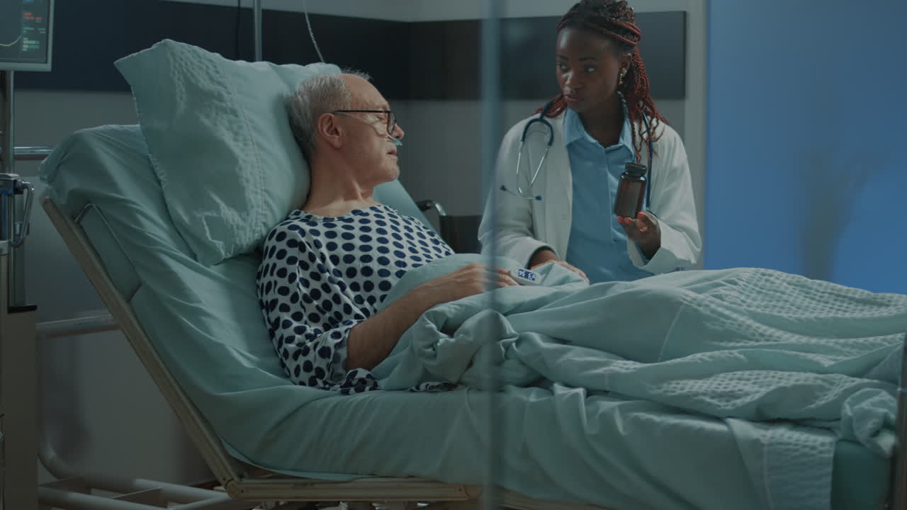 Medic at clinic giving pills to sick elder patient in hospital ward