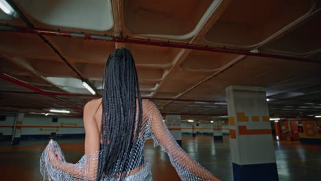 modish woman posing underground parking back view. brunette dancing shoulders