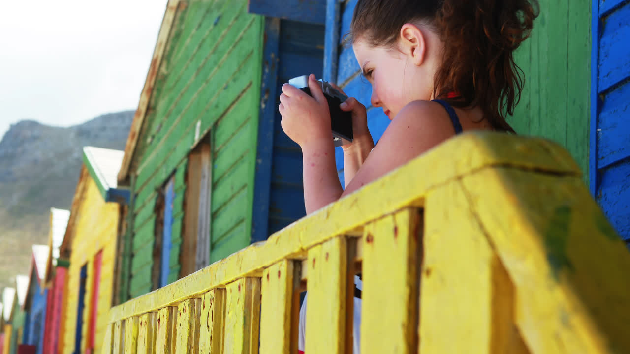 niña fotografiando con una cámara desde una colorida cabaña de playa