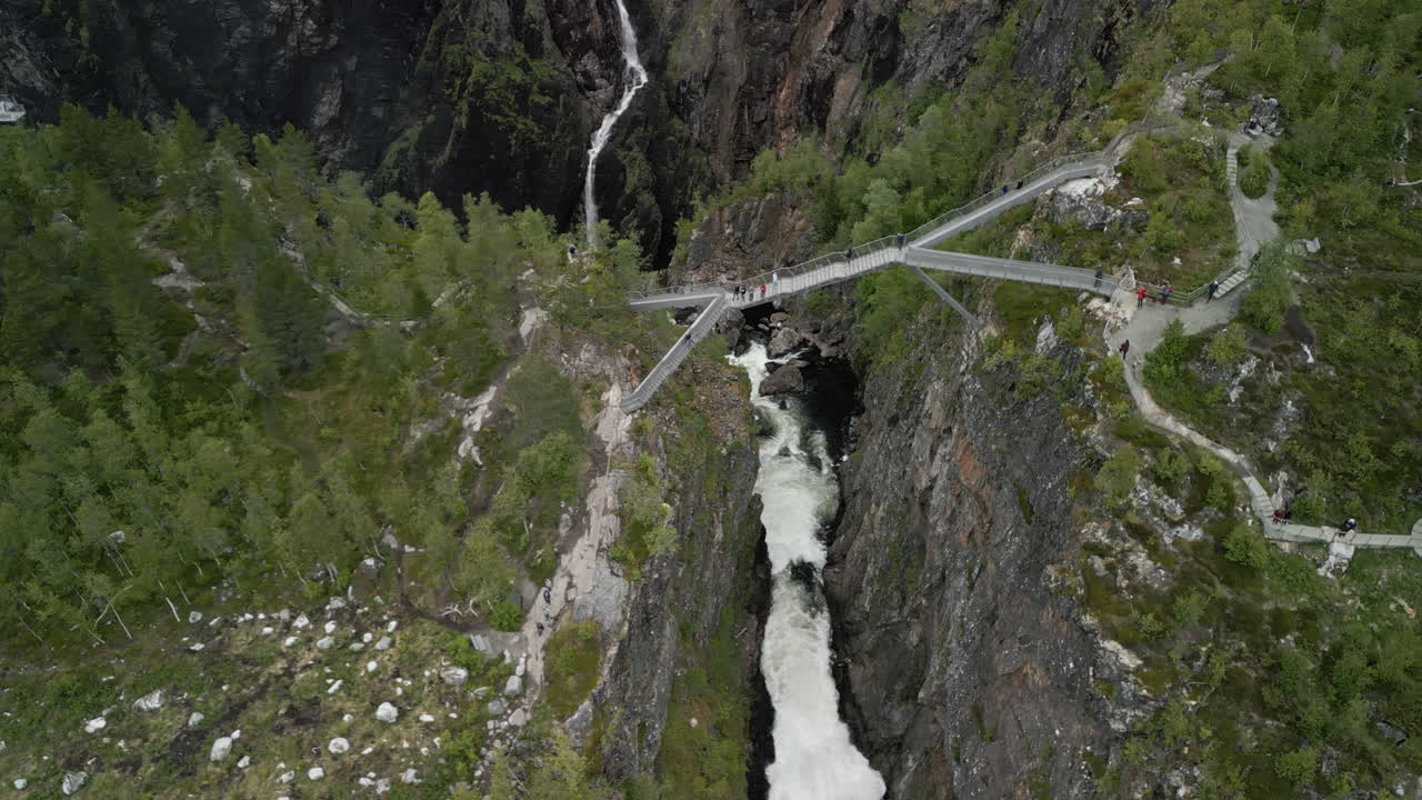 Drone shot of the bridge at the tourist attraction Vøringsfossen Waterfall in Norway. People walk across the bridge and cross a steep valley through which the water flows to the waterfall