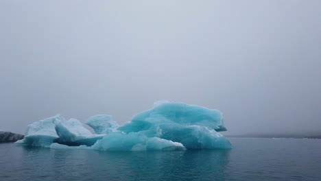 panning shot of bright blue iceberg floating in jokusarlon glacier lagoon, south iceland ring road highlights