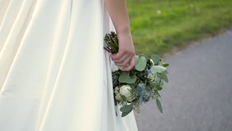 bride in wedding dress walks on road holds bouquet upside down dolly slow motion