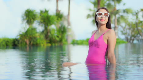 young asian girl with sunglasses and pink swimsuit relaxing in pool alone