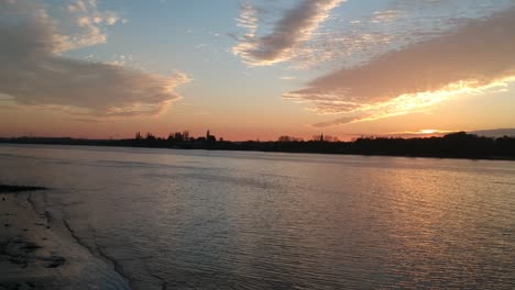 city silhouette on river coastline during golden hour, drone ascend view