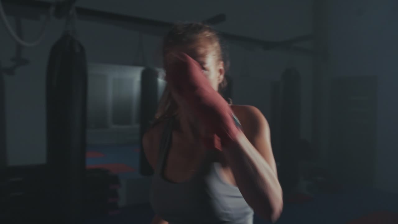 Boxeadora determinada treinando socos em uma academia escura