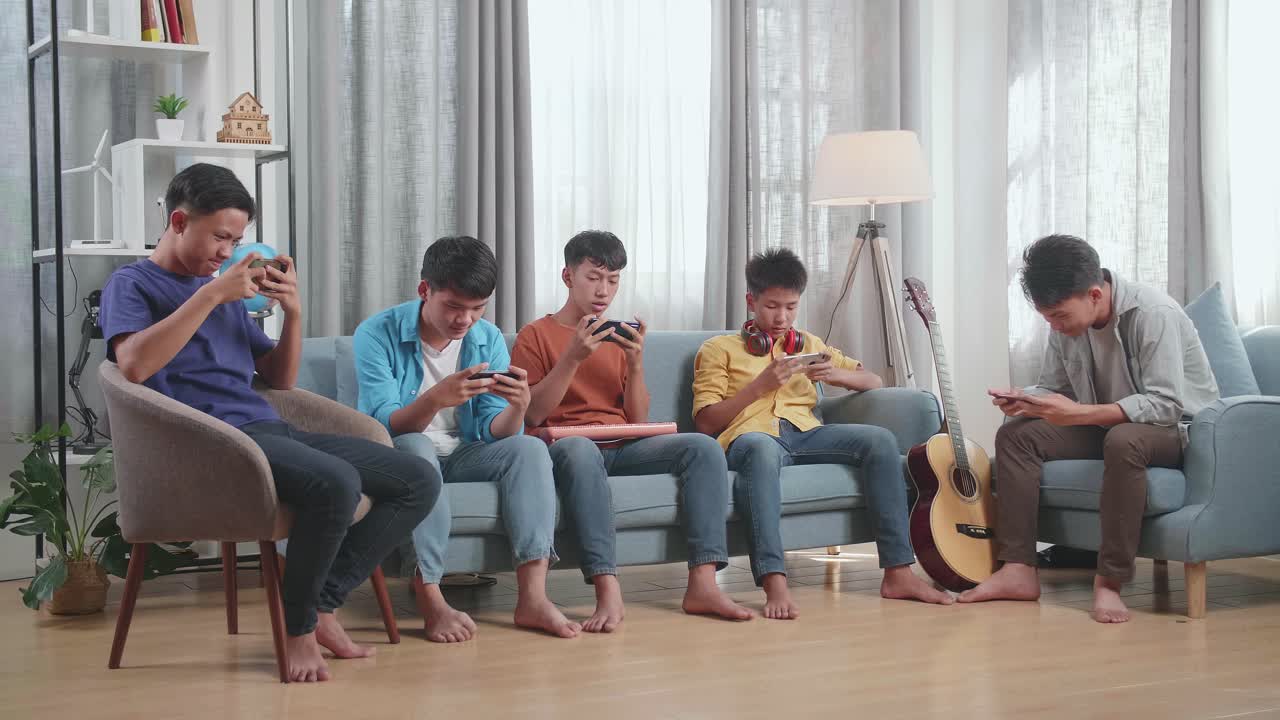grupo de jóvenes amigos asiáticos con instrumentos musicales jugando juntos en teléfonos inteligentes mientras están sentados en un sofá en casa