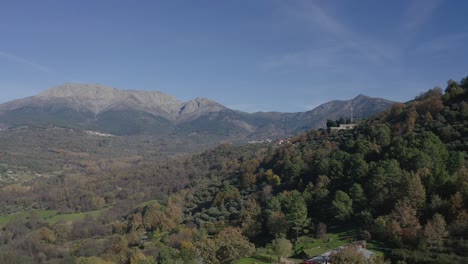 flight in a valley in autumn with colorful trees with pine and oak forests and some green meadow with a background of granite mountains and several towns on a day with blue sky in avila-spain