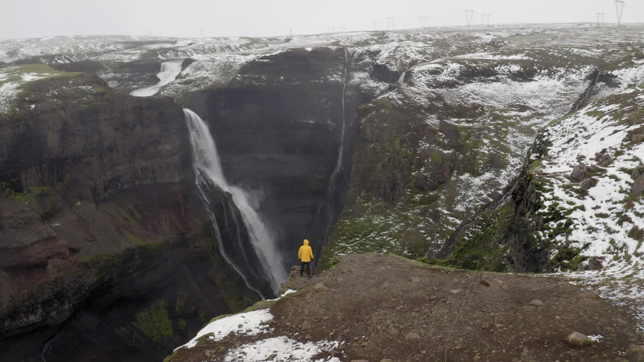 antena: toma panorámica lenta de un hombre parado cerca del borde de un acantilado, observando la cascada granni en islandia