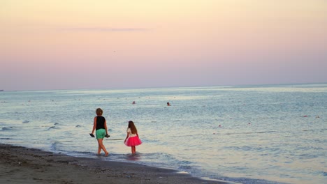 mother and daughter are walking in the sea water. back view of a woman and little girl walking in the evening on the blue sea water background.