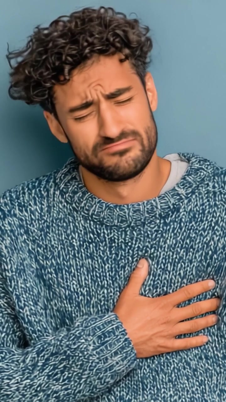 Un hombre expresando una emoción profunda mientras se agarra el pecho, mostrando un momento de introspección y vulnerabilidad sobre un fondo azul simple.