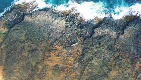 Aerial-tilt-up-from-volcanic-rocky-coast-to-open-blue-ocean-at-Hawaii