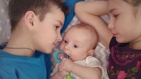 Siblings-kissing-newborn-brother.-Boy-and-girl-care-baby-Concept-of-kids-love