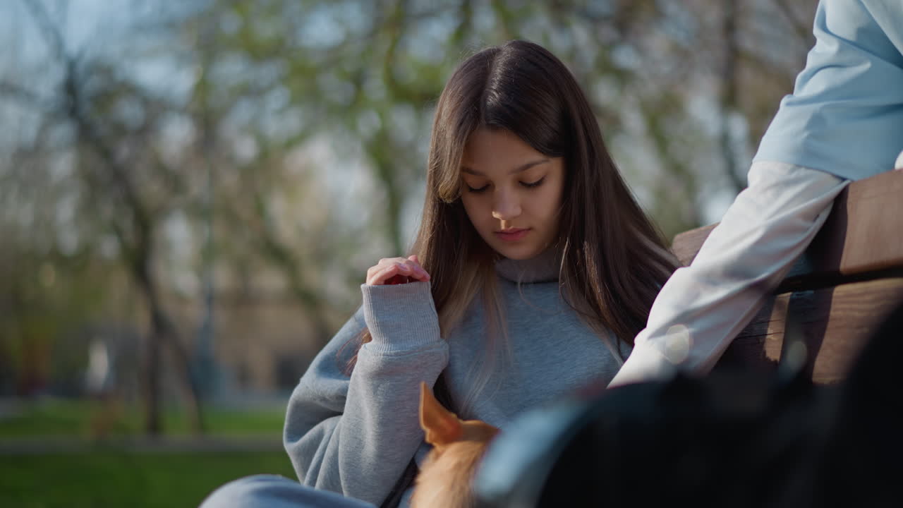 young female lovingly embraces small pet outside, teen girl gently interacts with tiny dog outdoors in park, adolescent girl expresses tender feelings while petting small chihuahua in park setting