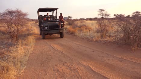 a safari jeep passes by at sunset on the plains of africa erindi park namibia with native tribal spotter riding on front