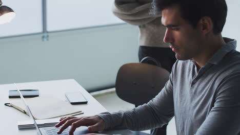 businessman working on laptop at desk joined by female colleague who collaborates on project