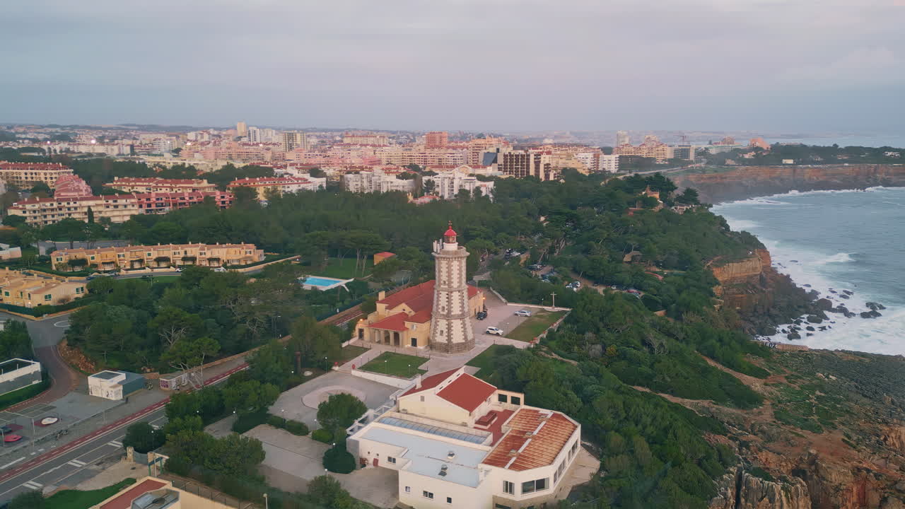 coastal town evening with lighthouse overlooking ocean drone view.