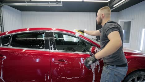 man worker washing red car on a car wash with yellow washcloth.